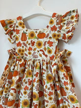 Load image into Gallery viewer, Yellow and orange autumn fabric showing pumpkins, sunflowers, birds, squirrels, and bunnies turned into a children&#39;s dress.
