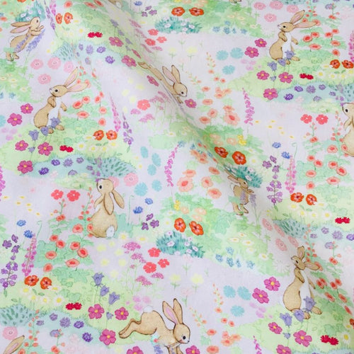 photo detail of boo's meadow fabric. the fabric has a pink background, and a repeat pattern of flowers and shrubs with bunnies jumping around. 